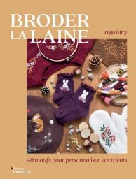 Couverture du livre « Broder la laine » d'Olga Uhry, aux tons beige et ocre. Photographie présentant des vêtements et accessoires en laine brodés : pull bordeaux à motifs floraux, chaussettes violettes ornées de lapins blancs, bonnet marron et moufles bla