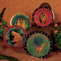 Set de 4 sous-verres collector Jurassic Park, motifs dinosaures et logos cultes, présenté en décoration sur fond sable et jungle.