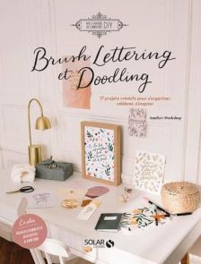 Couverture du livre "Brush Lettering et Doodling" montrant un bureau lumineux décoré de créations en calligraphie moderne.