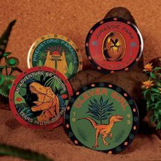 Set de 4 sous-verres collector Jurassic Park, motifs dinosaures et logos cultes, présenté en décoration sur fond sable et jungle.