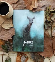 Couverture du livre "Nature illustrée" de Sandrot, photographiée sur un lit de feuilles d'automne avec une tasse de café. L'illustration douce et poétique présente une aquarelle de biche se fondant dans une brume aux teintes vert d'eau et bleutées.